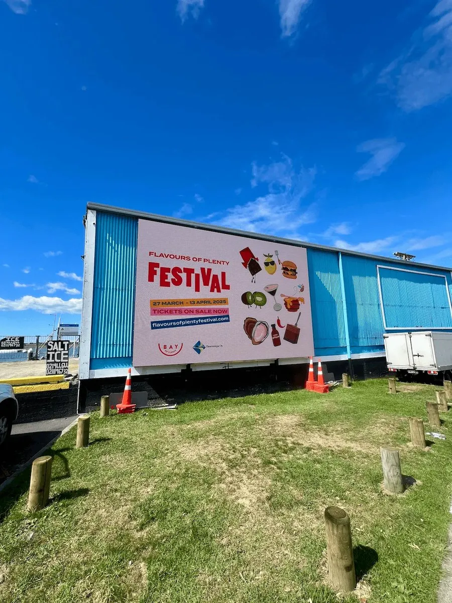 A Flavours of Plenty Festival billboard on the side of a building under a blue sky