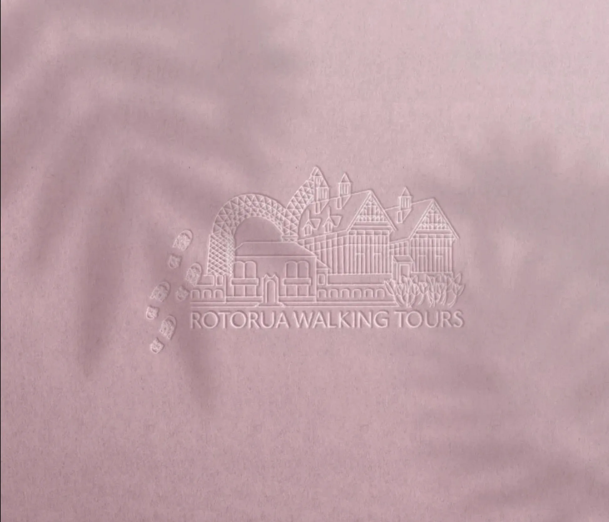 The Rotorua Walking Tours logo, an illustrated row of Rotorua landmarks and footprints, embossed on pink paper.