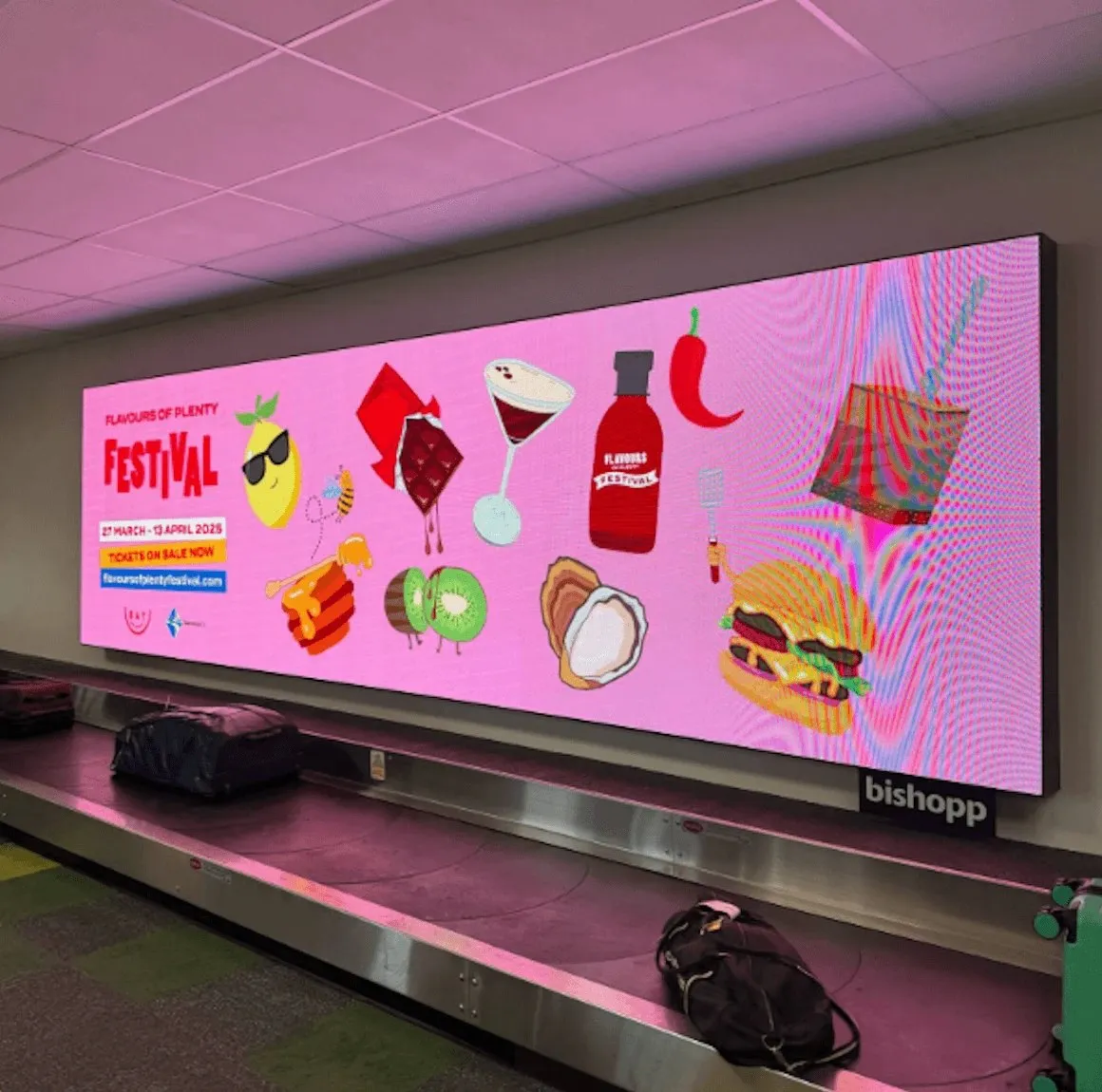 The festival campaign on a large digital screen above a baggage carousel at the airport.