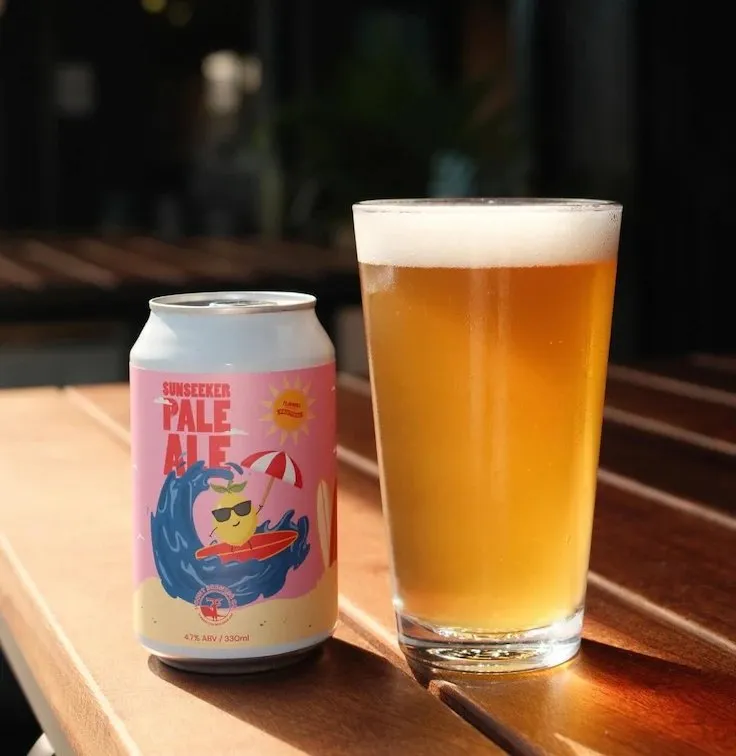 The Sunseeker Pale Ale can beside a full glass on a sunny table.
