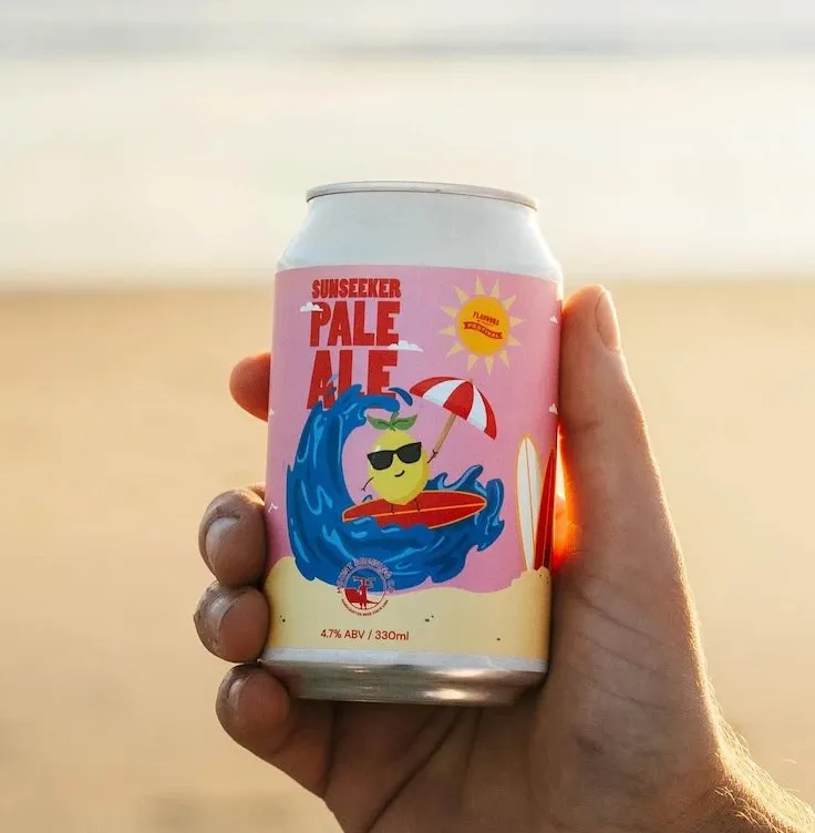 A hand holding the Sunseeker Pale Ale can at the beach.